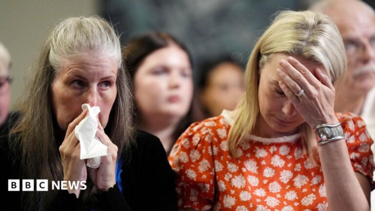 Sarah Hawkins holds a tissue to her face and appears tearful. Sarah Hawkins, sitting next to her, holds her hand to her forehead.