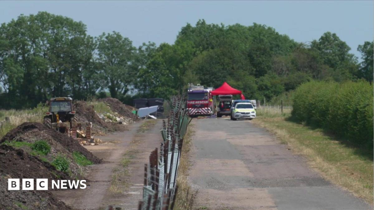Emergency services parked at the end of a pavement next to fields. There is a fire engine and a police car.