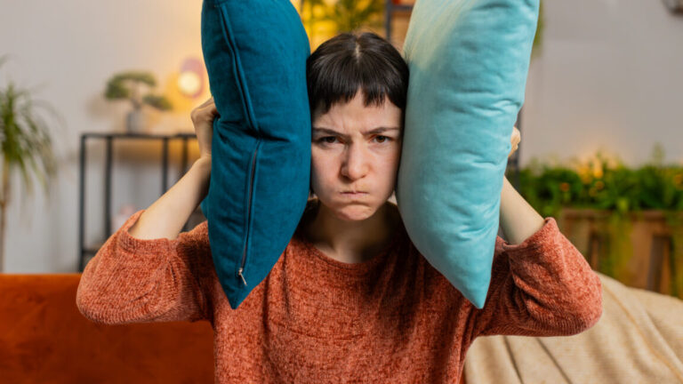 Irritated woman covers ears with cushions