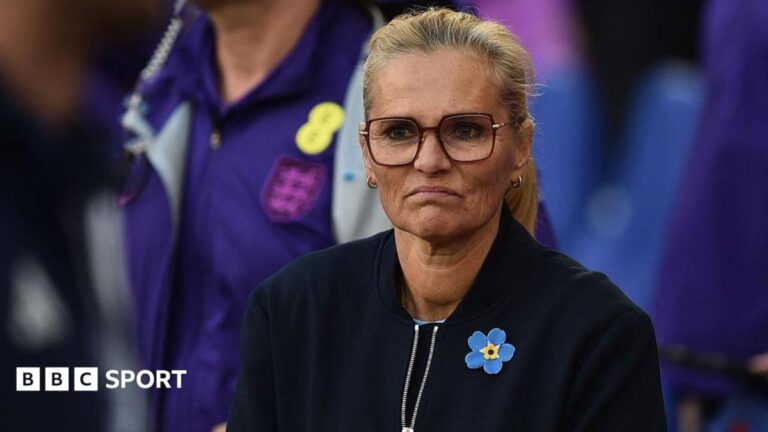 A frowning Sarina Wiegman in dark top and yellow and blue broach