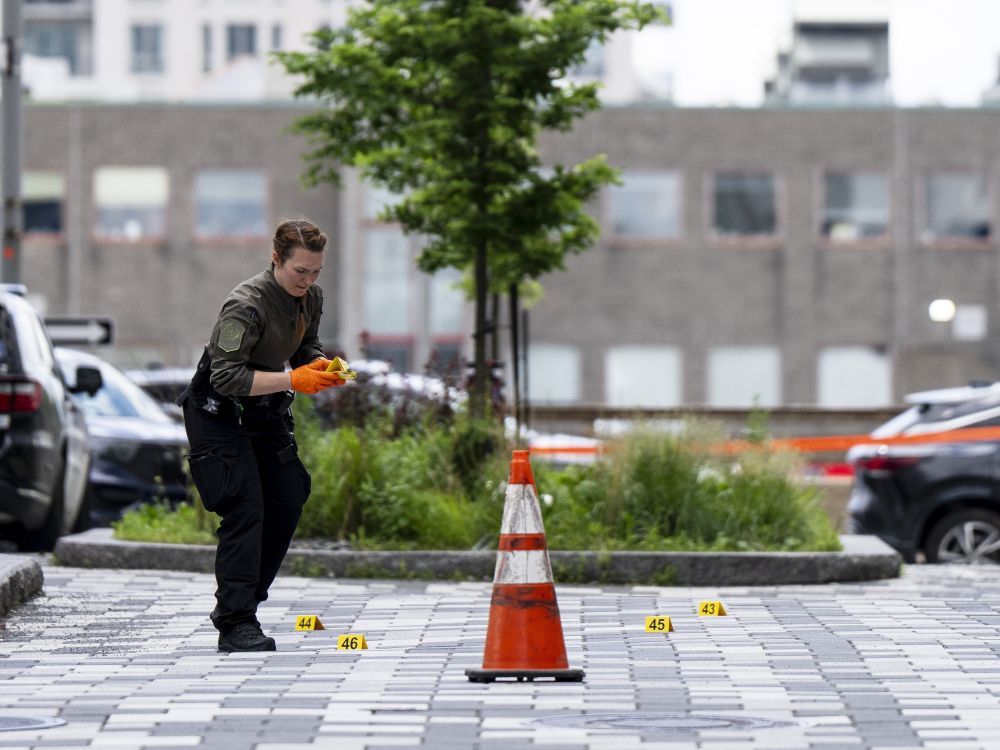A uniformed police officer places numbered yellow evidence markers on a sidewalk.