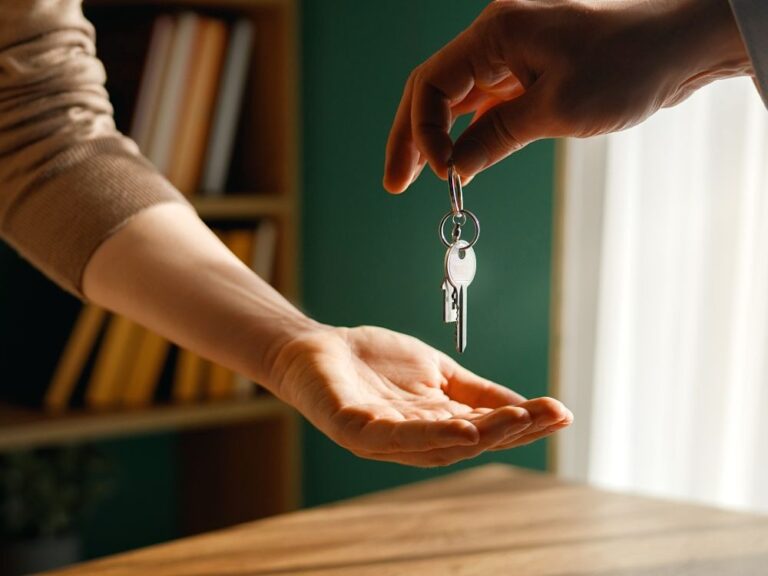 One person's hand drops a house key into the hand of another person.