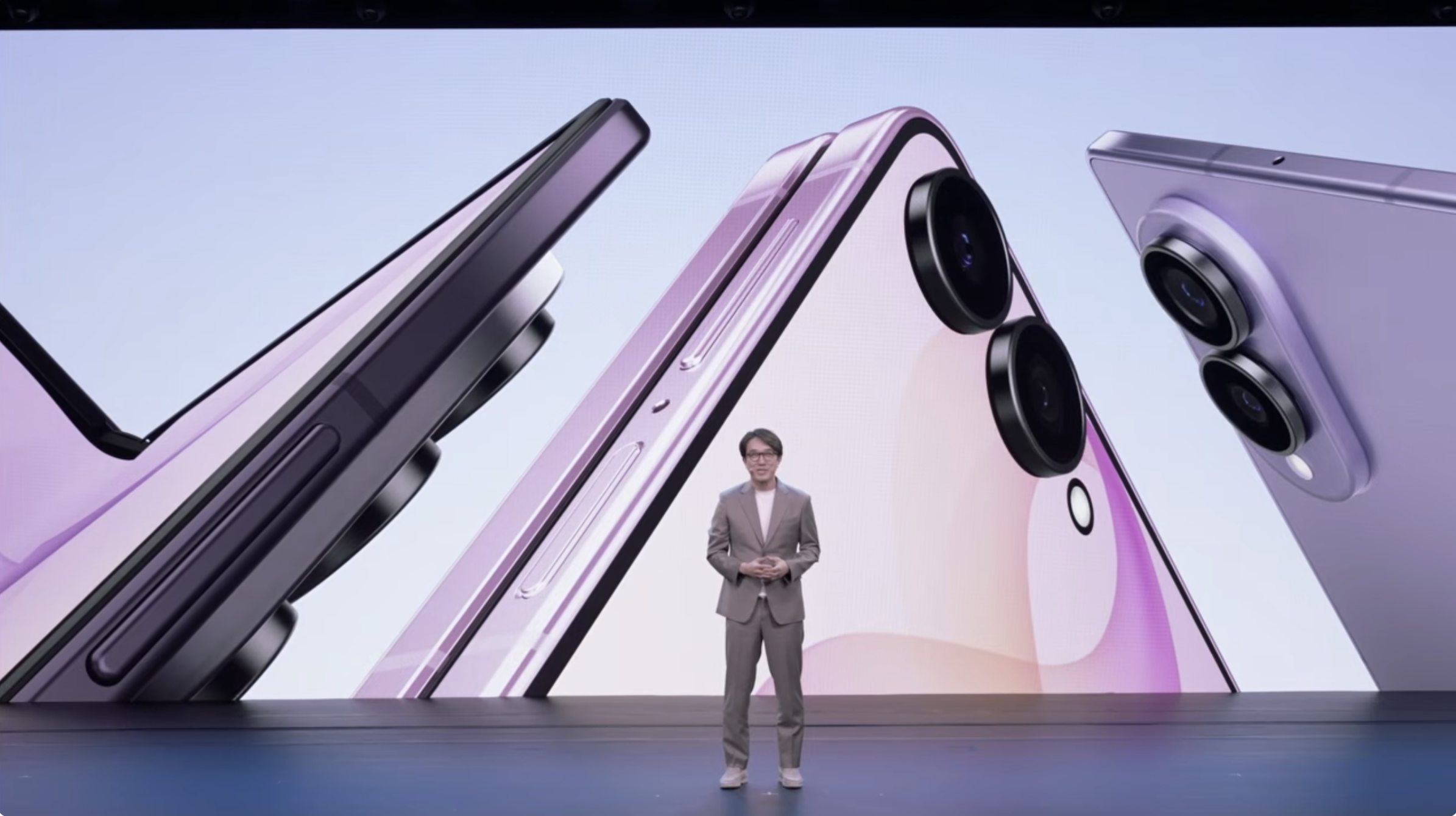 A man on stage in front of a large screen depicting foldable phones.