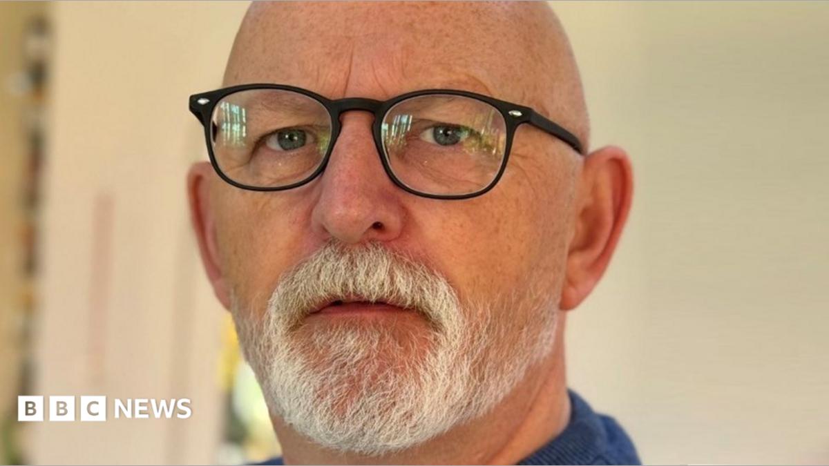 A bald man with a white beard is wearing glasses
