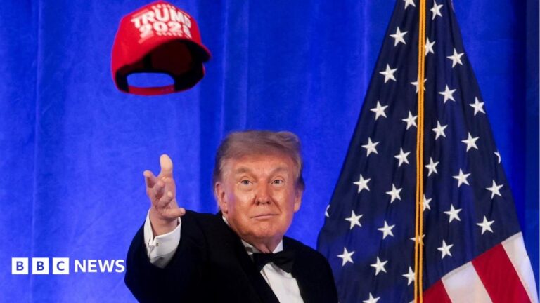 Trump in bow tie, before American flag, tosses red "Trump 2028" cap in air
