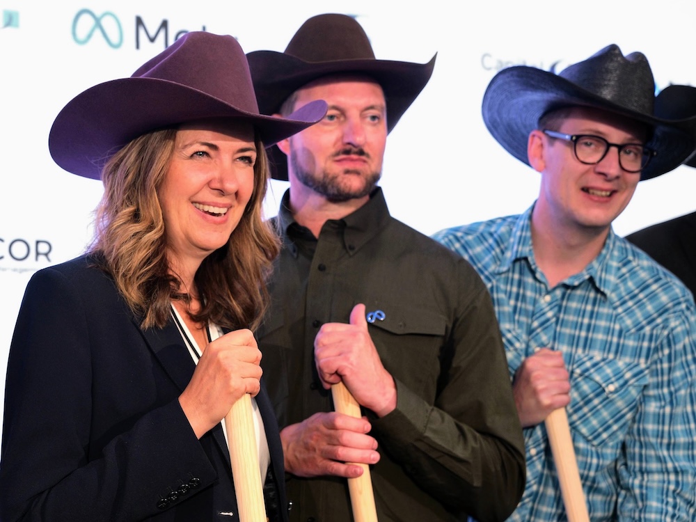 Danielle Smith and two middle-aged light-skinned men pose holding shovels. They are wearing cowboy hats.
