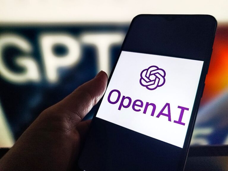 A phone with an OpenAI logo held next to a ChatGPT sign.