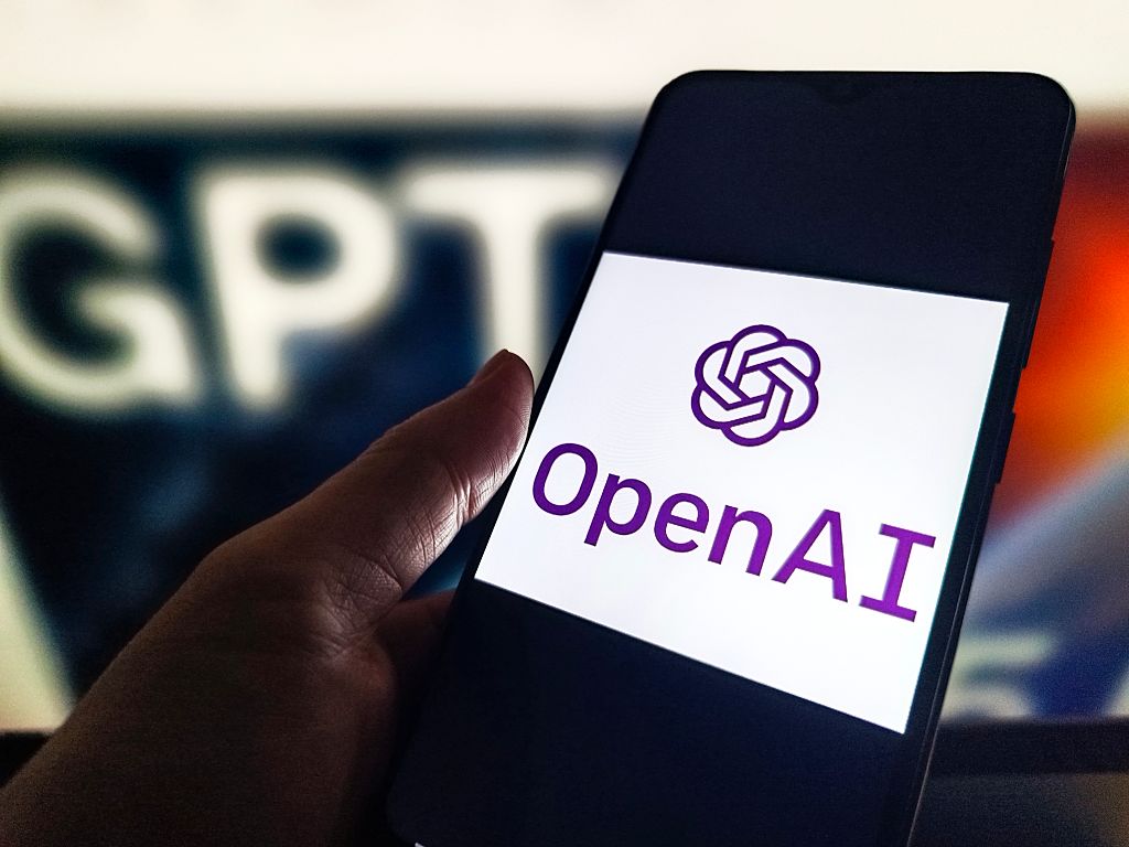 A phone with an OpenAI logo held next to a ChatGPT sign.