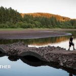 View of a depleted reservoir with a boy walking across a bridge with a fishing rod