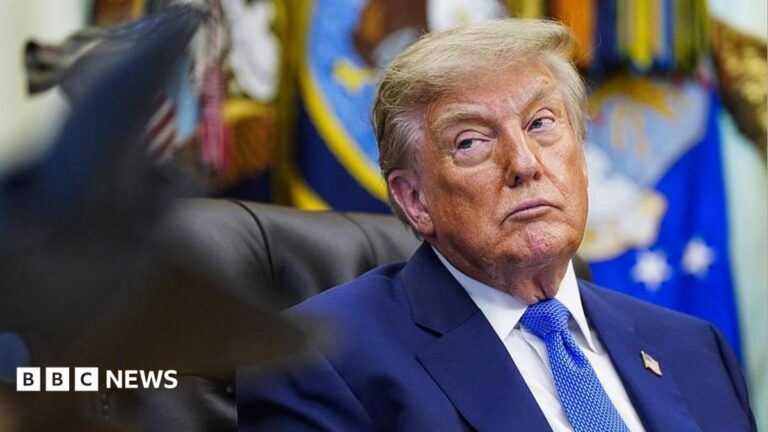 Donald Trump glances to his right while seated at his desk in the Oval Office.