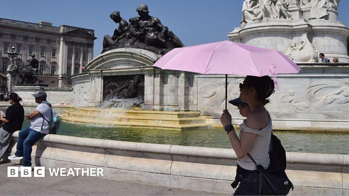 two people under an umbrella shading themselves from the strong summer sunshine walking in front of a fountain at Buckingham Palace