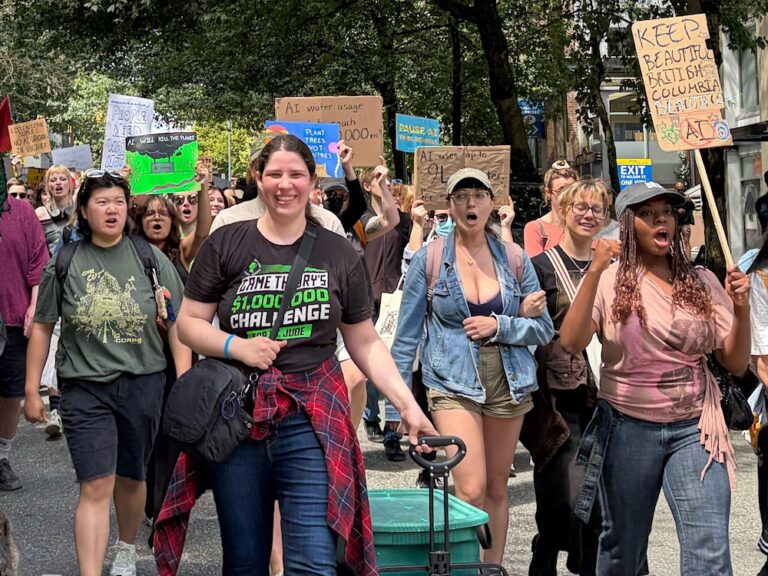 A group of people hold signs opposing an AI data centre as they march down a street in Vancouver.