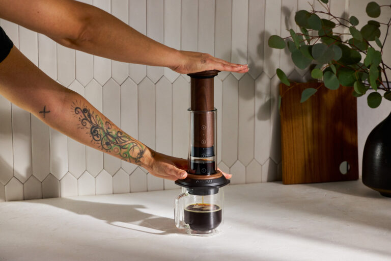 A hand pushing down on the walnut AeroPress brewer.