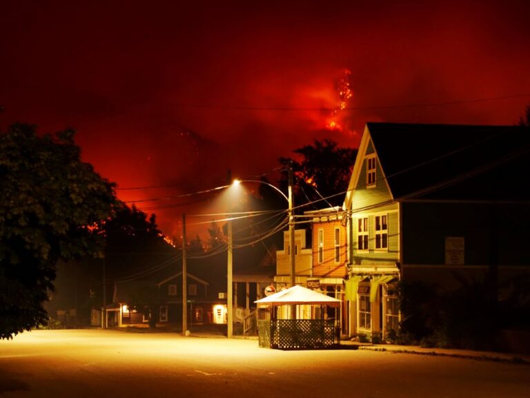 A quaint streetscape at night sits in front of a backdrop of a red, fiery mountain.
