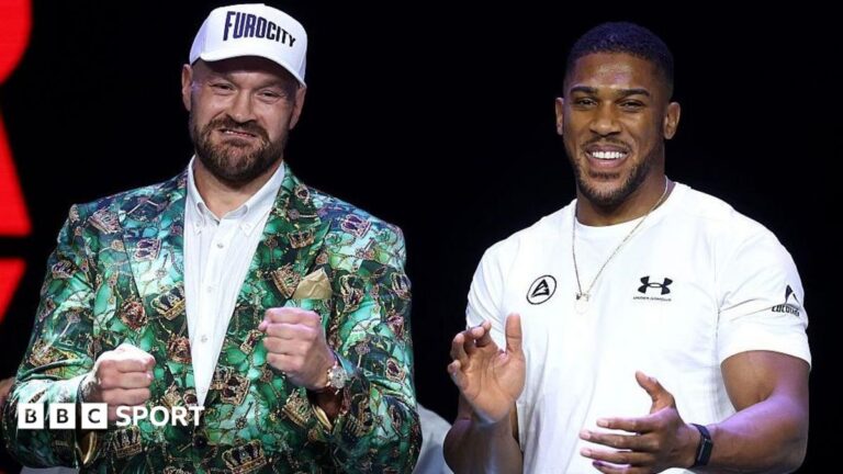 Tyson Fury holds up his fists and Anthony Joshua holds up his hands and smiles