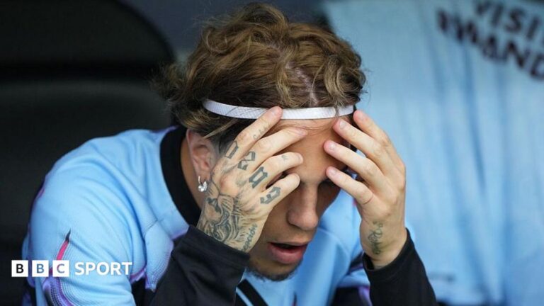 Alejandro Garnacho, wearing a light blue training top and white headband, has his tattooed hands held up to his forehead while looking downwards