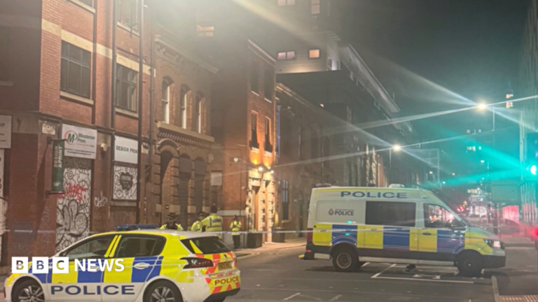 A police car and a van and several officers stand guard by a police cordon in a city-centre location.