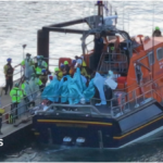 People wrapped in blankets on the back of an RNLI lifeboat moored by a pontoon at Eastney, Portsmouth, on 6.9.26