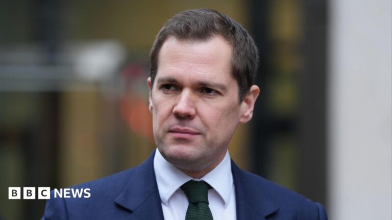 Robert Jenrick is wearing a blue suit jacket, white shirt and green tie.