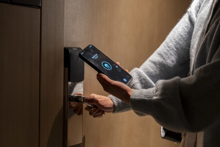 A person using a phone app to unlock a smart lock on a wood door.