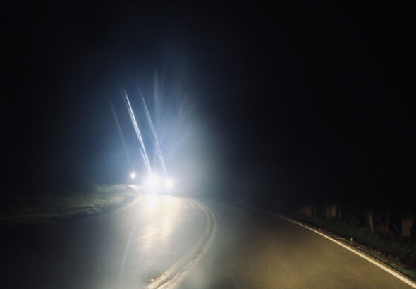 From the perspective of the driver, headlights shine brightly from oncoming traffic at night.